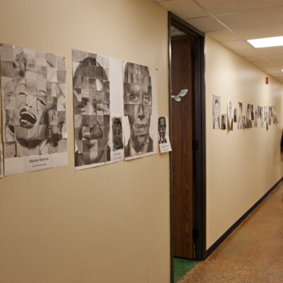Male teacher walks down a hallway with student art at La Academia de Esperanza