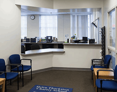 An administrative office with white walls a built in desk and blue chairs