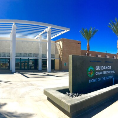 A large school building in the background with a water feature in foreground reading "Guidance Charter School Home OF The Gators'