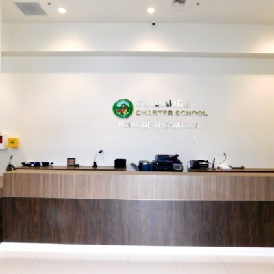 A wooden front desk with a sign above saying "Guidance Charter School Home Of The Gators