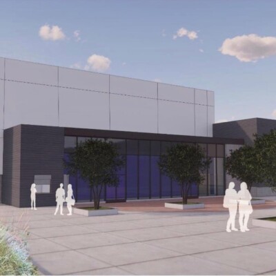 Modern building entrance with people walking outside on a sunny day.